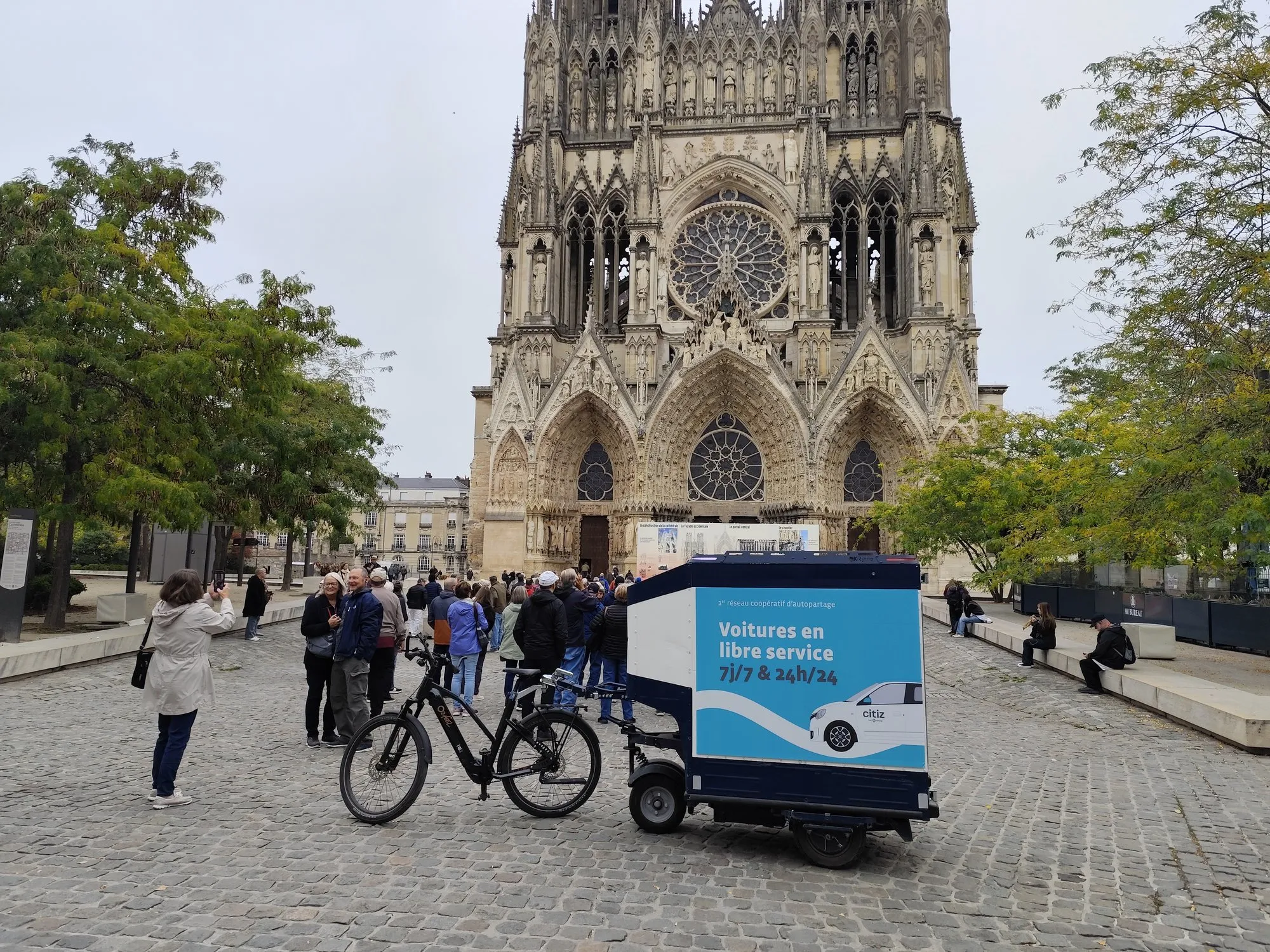 Vélo publicitaire LCDG stationné sur le parvis de la cathédrale de Reims au milieu des visiteurs