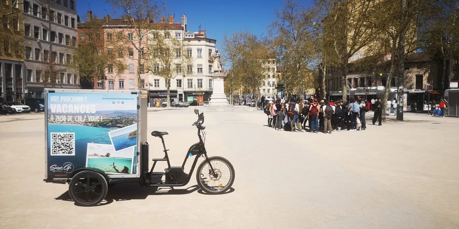 Vélo publicitaire LCDG sur une grande place piétonne très fréquentée